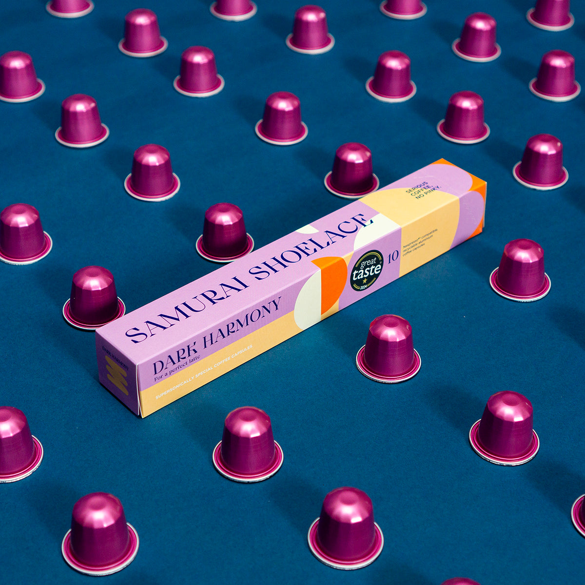 Samurai Shoelace Serious Coffee Dark Harmony kávékapszula termékfotója kék háttérrel rózsaszín kapszulákkal